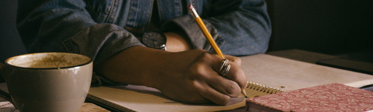 Person writing in a notebook. Photo by Kat Stokes on Unsplash