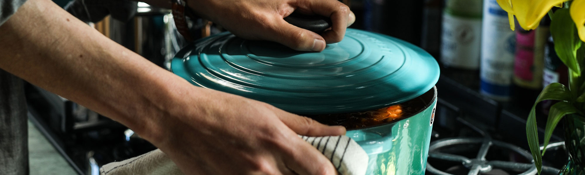 Person in a kitchen holding a large casserole dish, next to a gas cooker.