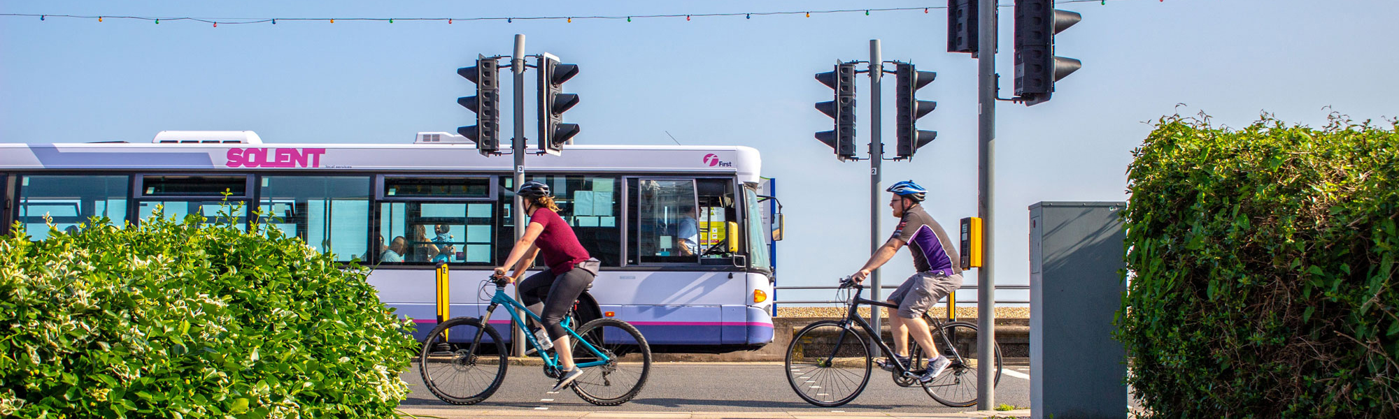Two cyclists on a seafront road, with a single-decker bus on the other side of the road