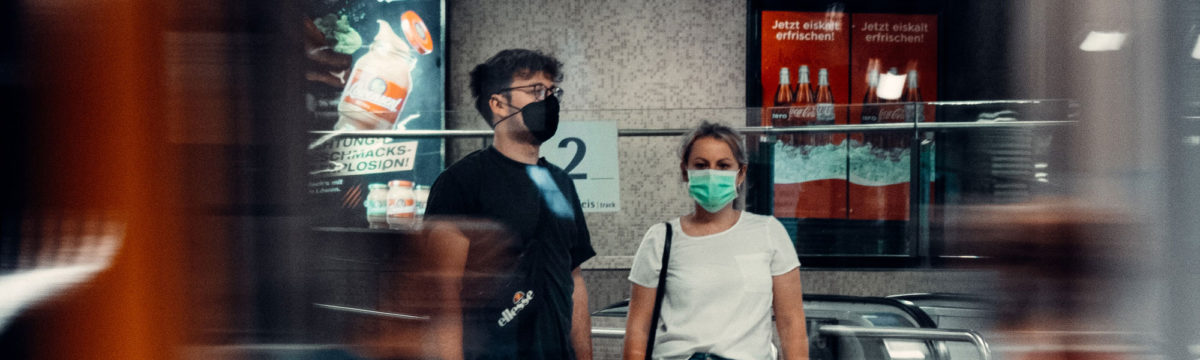 Two people wearing face coverings, standing in front of an escalator