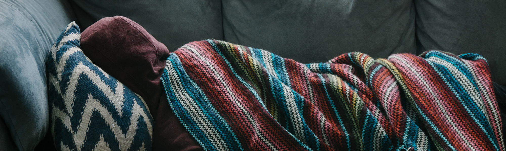 Young man asleep on sofa with blanket and hood. Photo by Rex Pickar on Unsplash