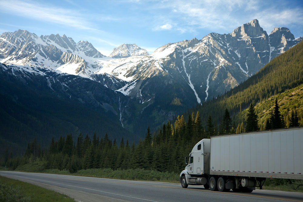 Large articualted truck on a highway amongst snow-capped mountains and conifer forest